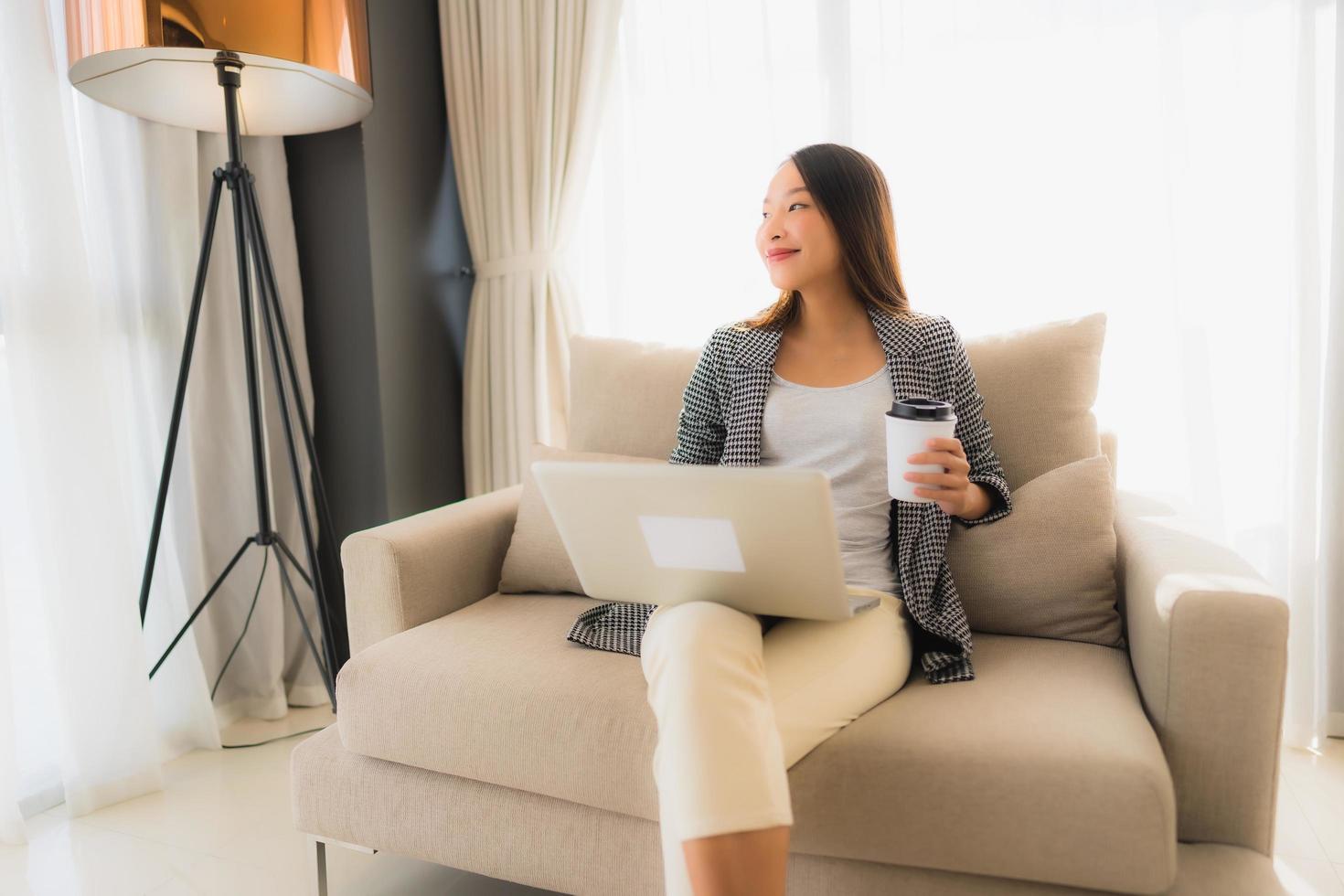 Beautiful young asian portrait using computer and laptop with coffee cup sitting on sofa photo