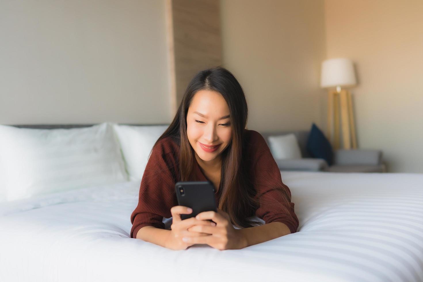 retrato, hermoso, joven, mujeres asiáticas, utilizar, teléfono móvil, en cama foto