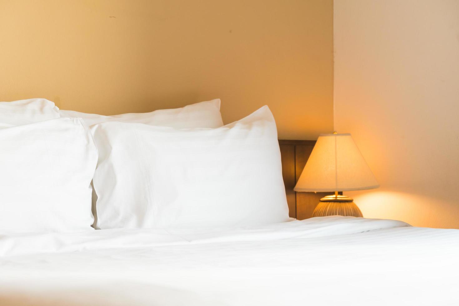 White comfortable pillow on bed with light lamp photo