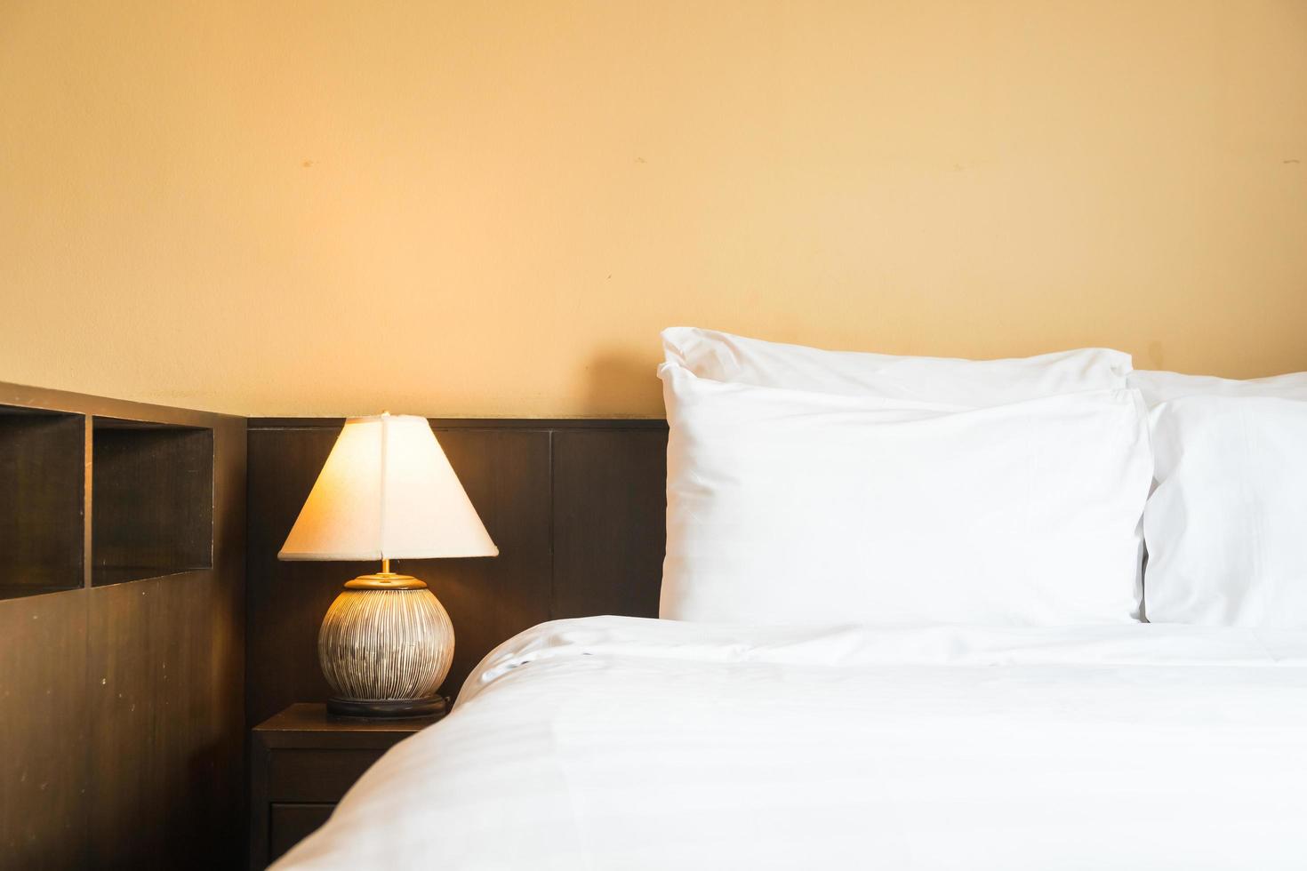 White comfortable pillow on bed with light lamp photo