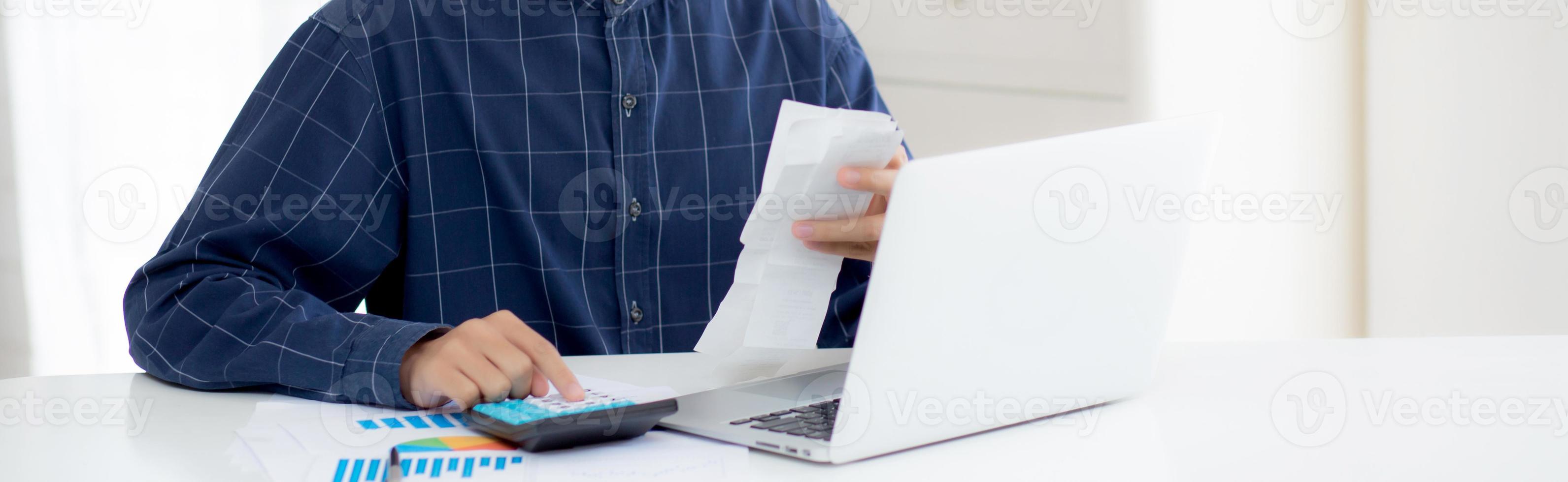 Hombre asiático joven que calcula el hogar de las finanzas con la calculadora en el escritorio en casa, la cuenta de control masculina y el éxito para ahorrar gastos del hogar, cierre de la deuda, impuestos y contabilidad, concepto de negocio foto