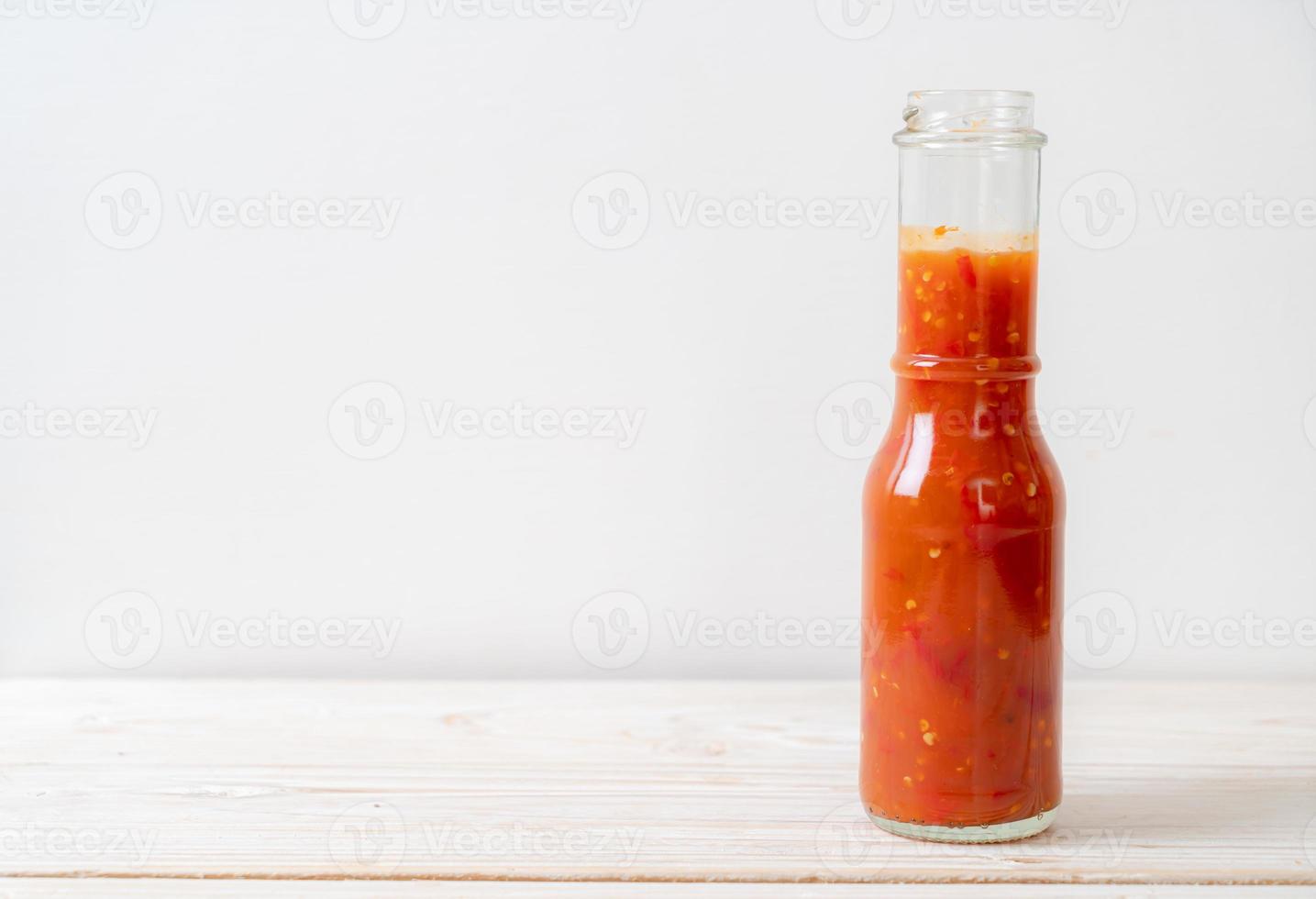 Chili or chili sauce in bottle and jar on wood background photo