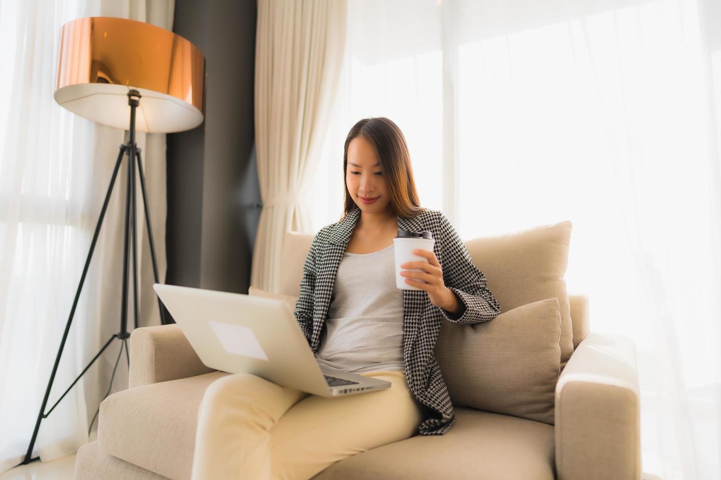 Beautiful young asian portrait using computer and laptop with coffee cup sitting on sofa photo