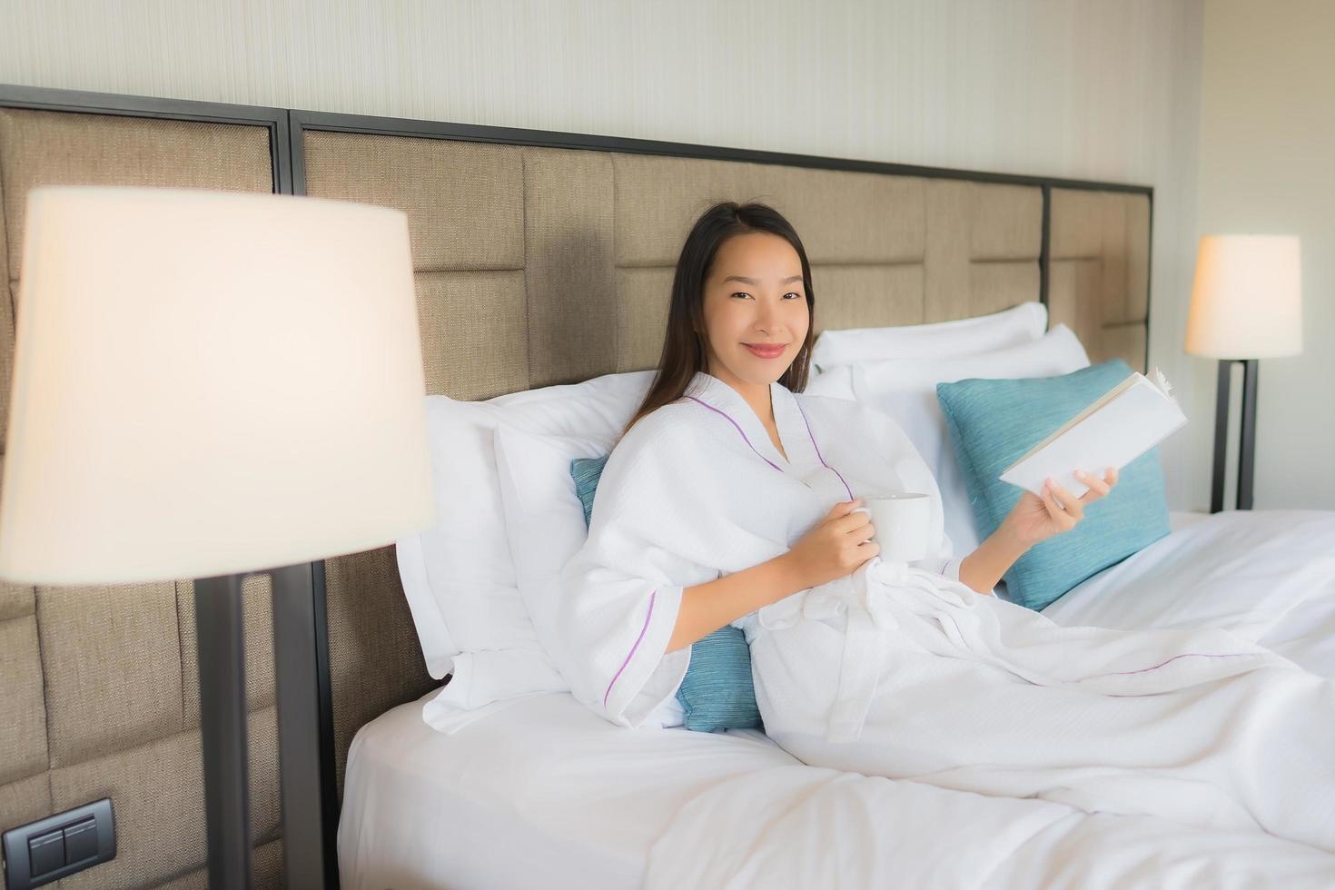 Portrait beautiful young asian women with coffee cup and book on bed photo