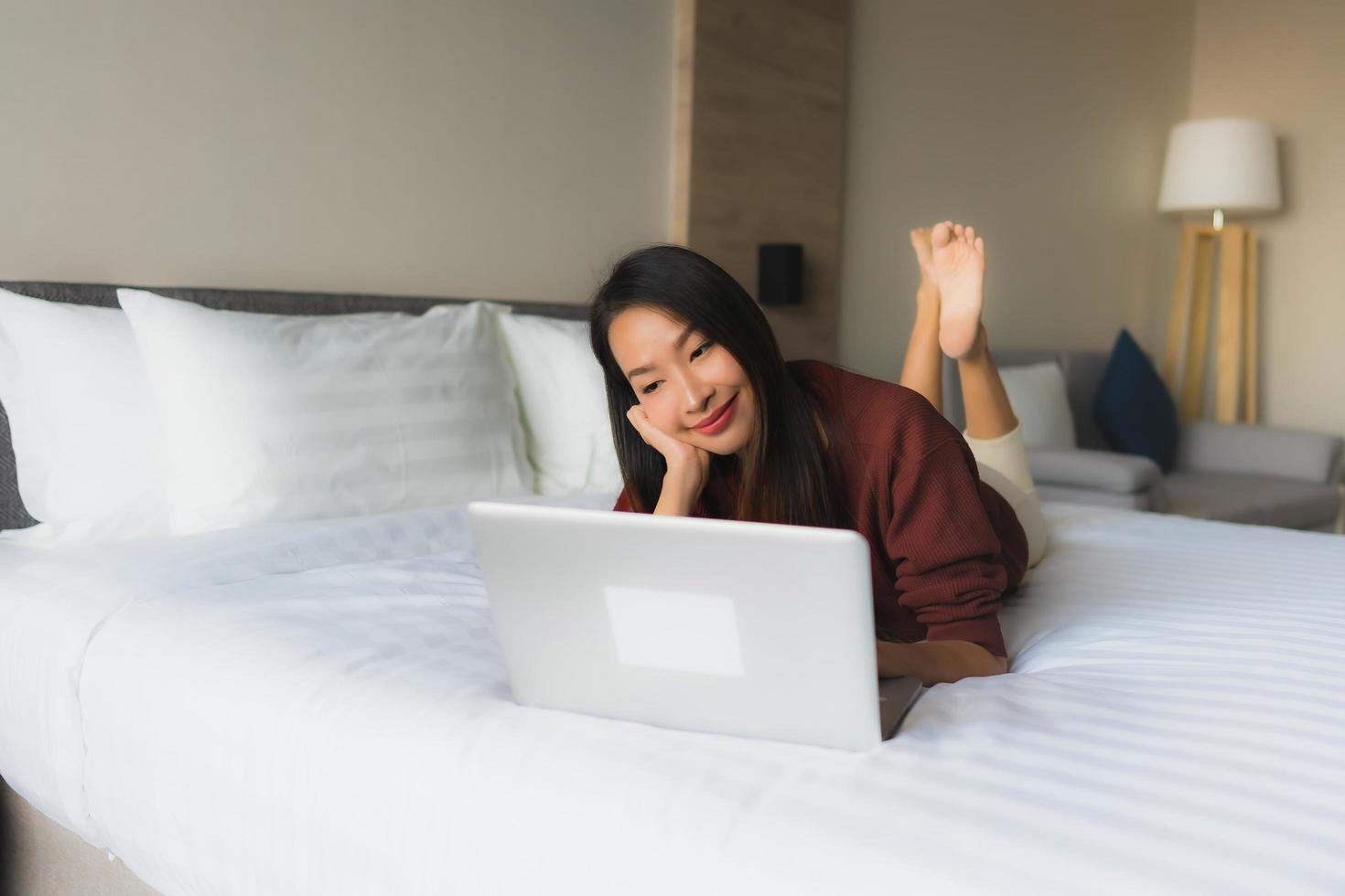 retrato, hermoso, joven, mujeres asiáticas, utilizar, computadora, y, teléfono móvil, en cama foto