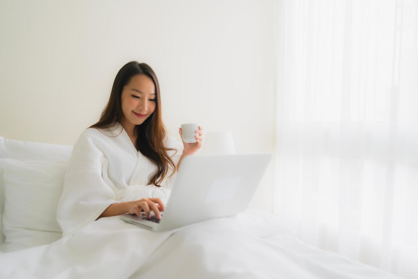 Portrait beautiful young asian women with coffee cup and computer laptop on bed photo