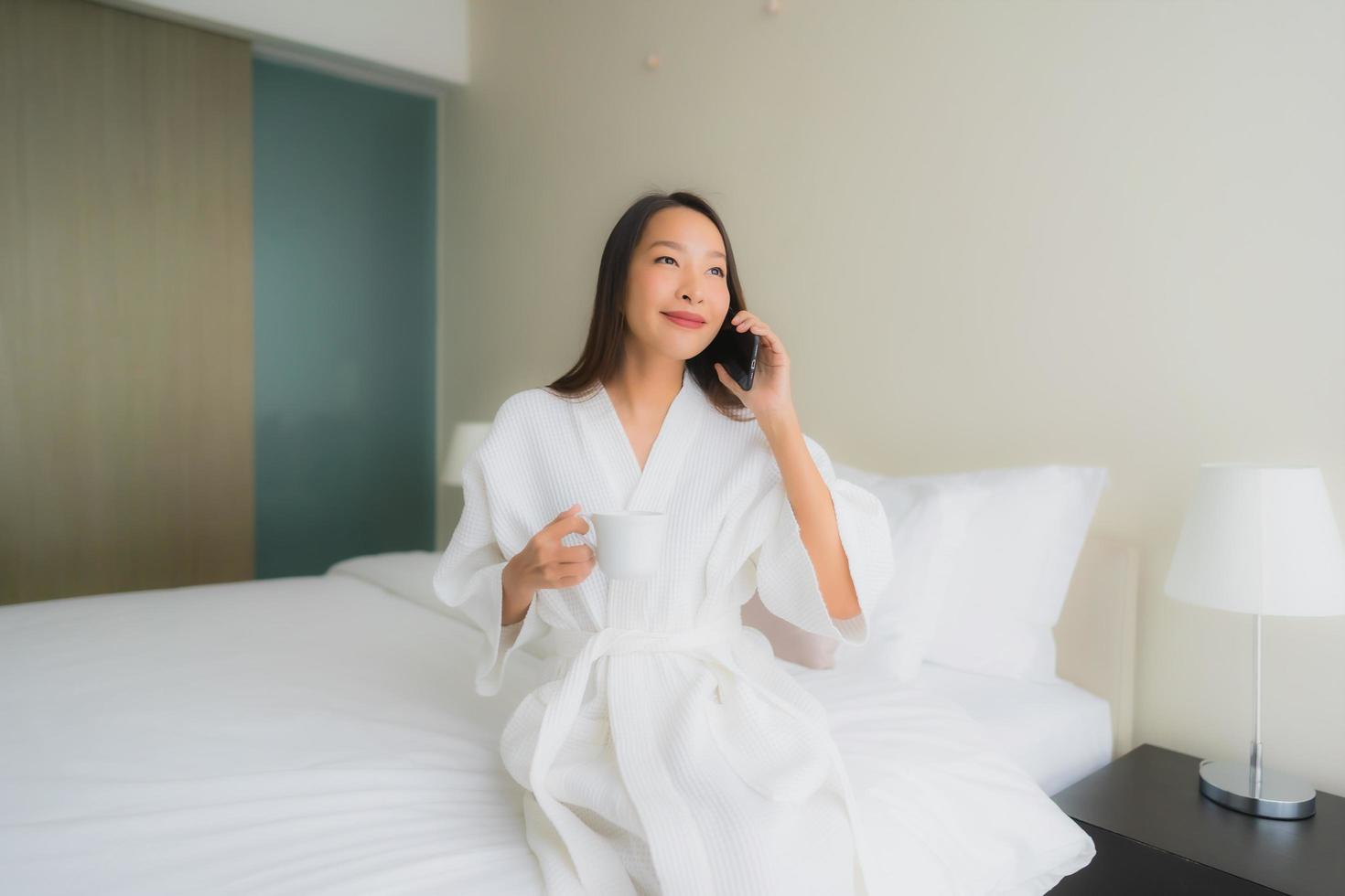 retrato, hermoso, joven, mujeres asiáticas, con, taza de café, y, teléfono móvil, en cama foto