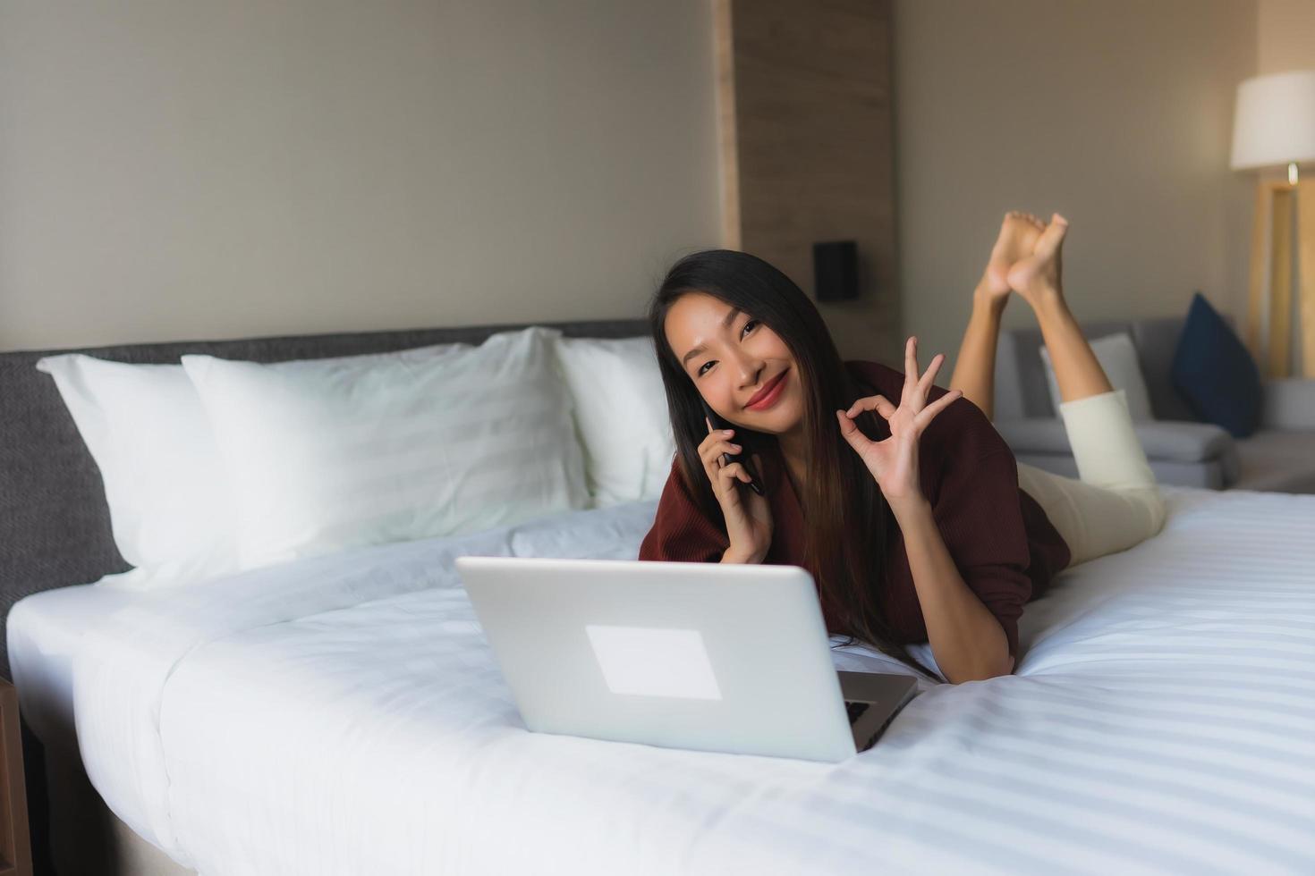 retrato, hermoso, joven, mujeres asiáticas, utilizar, computadora, y, teléfono móvil, en cama foto
