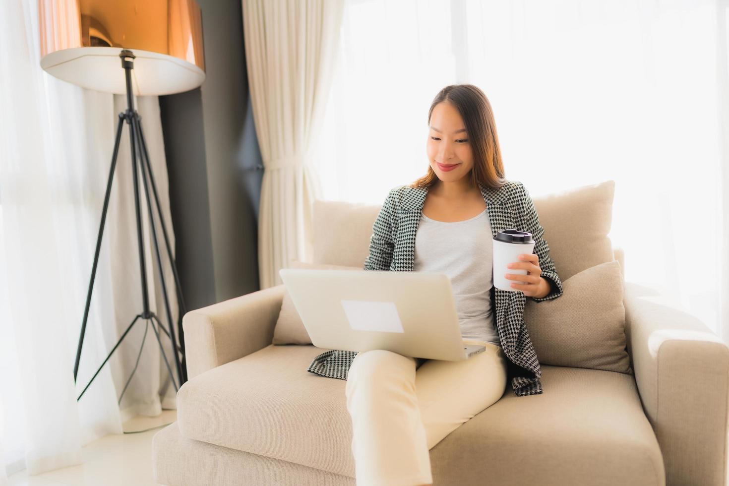 Beautiful young asian portrait using computer and laptop with coffee cup sitting on sofa photo