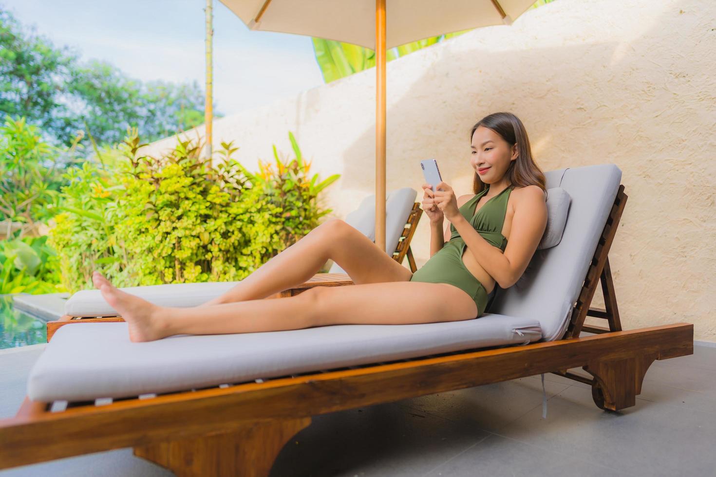 Portrait beautiful young asian woman sitting on the chair deck with umbrella neary swimming pool photo