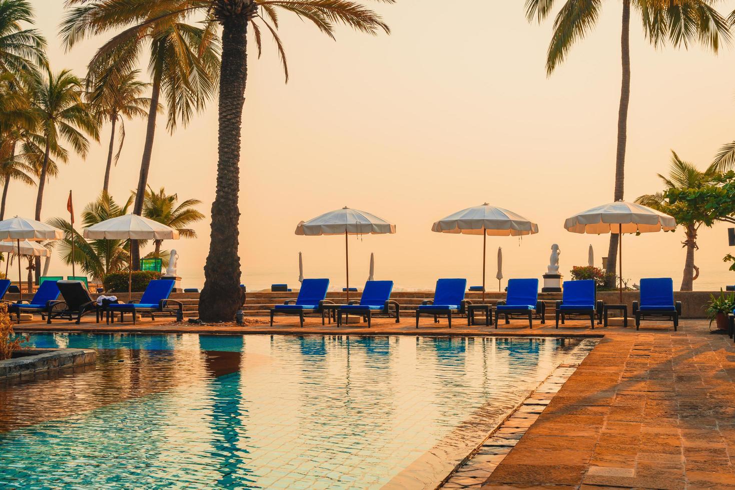 Hermosa palmera con sombrilla piscina en hotel resort de lujo al amanecer - concepto de vacaciones y vacaciones foto