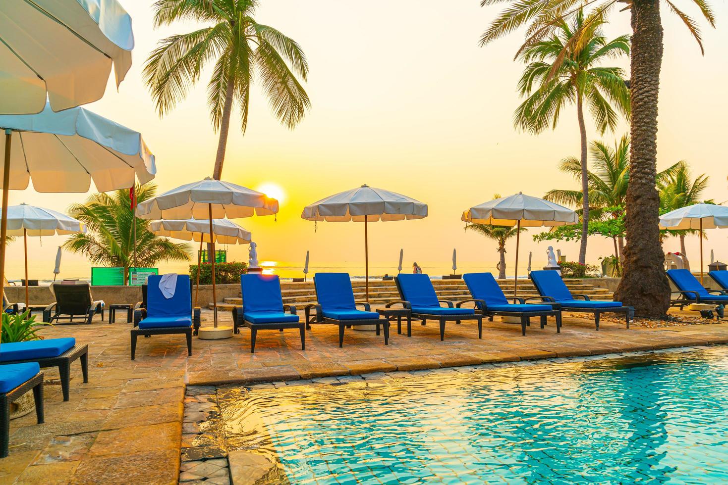 Beautiful palm tree with umbrella chair pool in luxury hotel resort at sunrise times - holiday and vacation concept photo