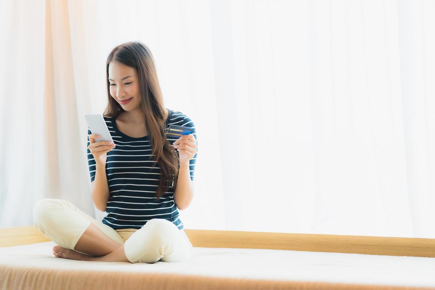 Retrato joven y bella mujer asiática mediante teléfono móvil o inteligente con tarjeta de crédito para ir de compras en el sofá foto