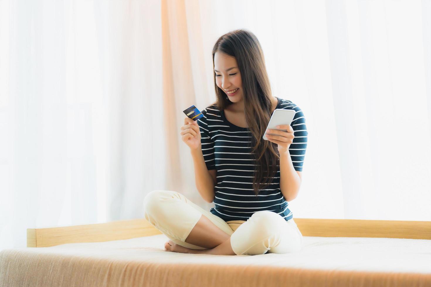 Retrato joven y bella mujer asiática mediante teléfono móvil o inteligente con tarjeta de crédito para ir de compras en el sofá foto