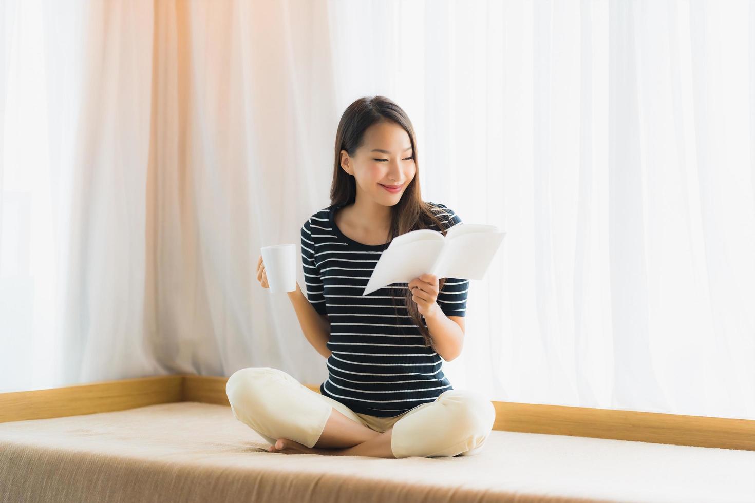 Portrait beautiful young asian woman reading book and hold coffee cup or mug in on sofa in living room area photo