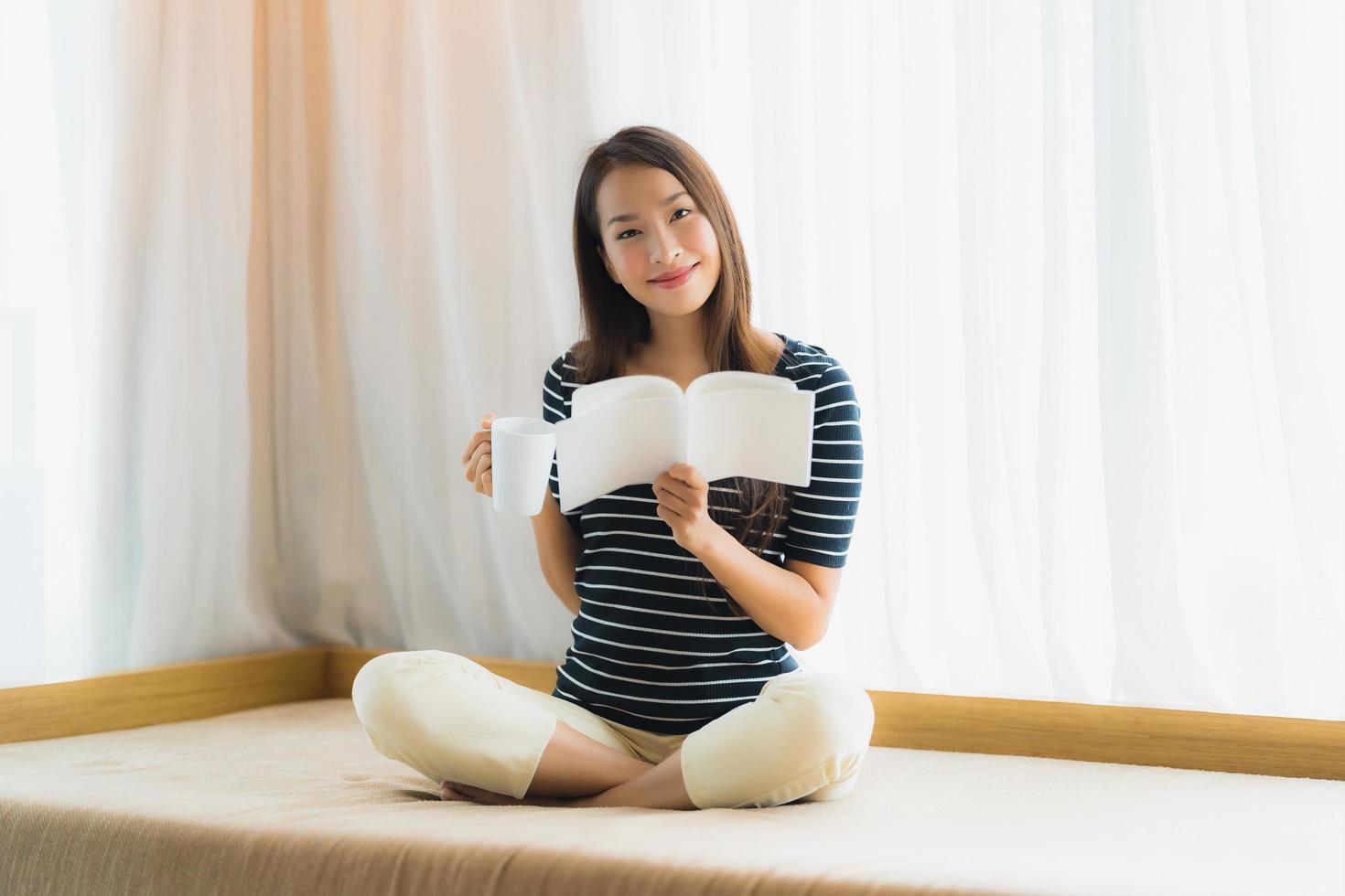 Portrait beautiful young asian woman reading book and hold coffee cup or mug in on sofa in living room area photo