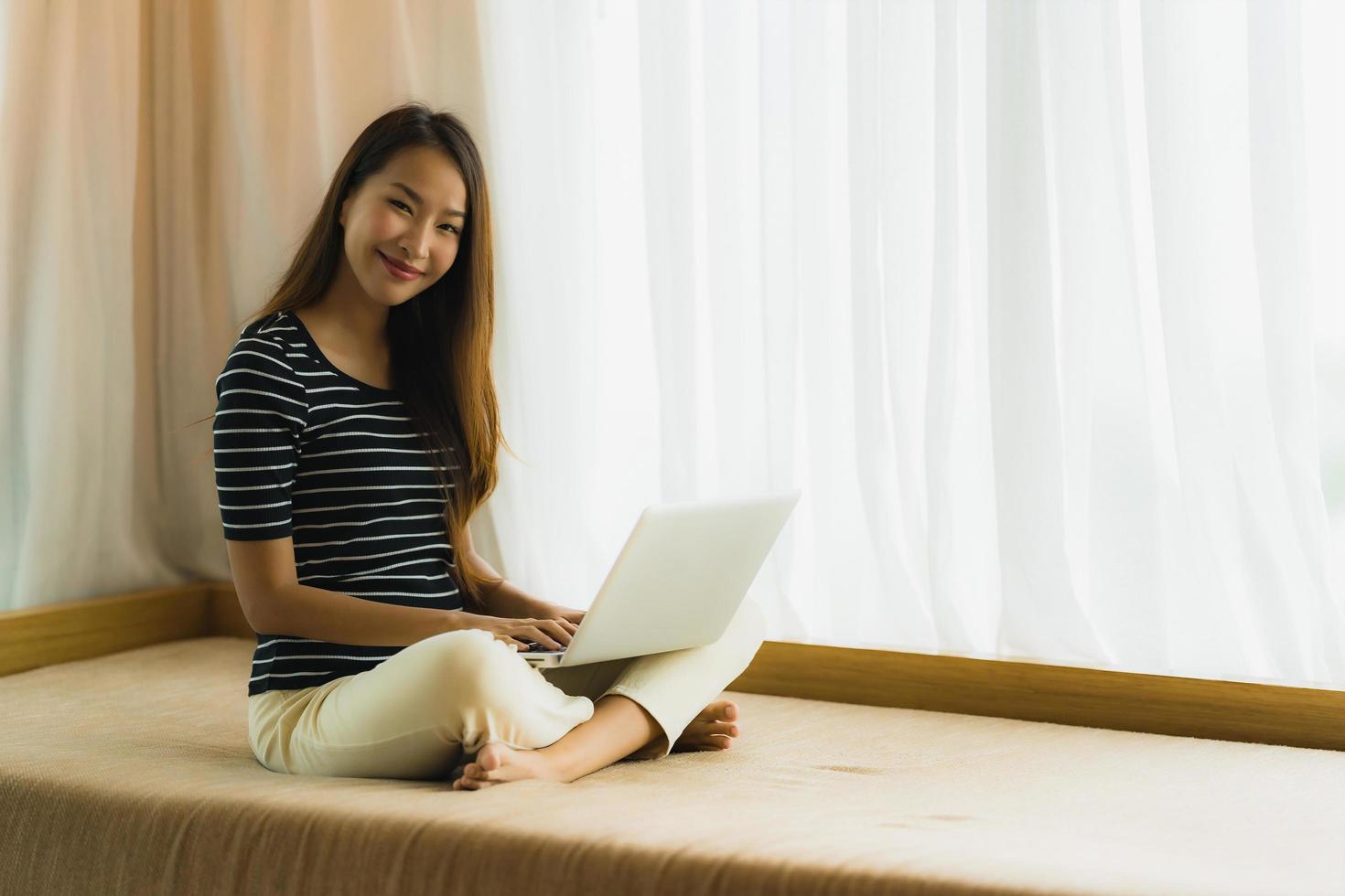 Portrait beautiful young asian woman using computer notebook or laptop on sofa in living room photo