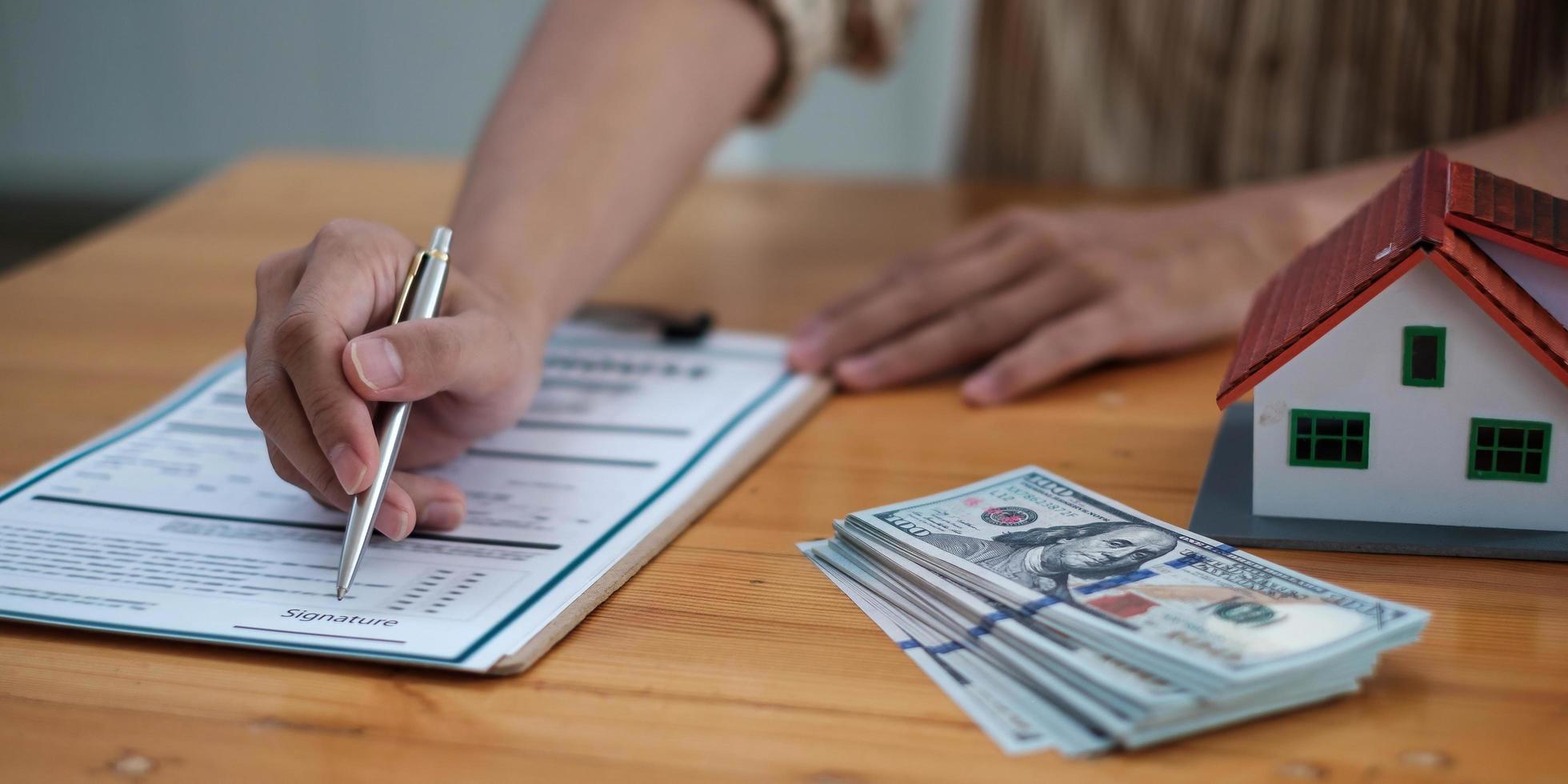 Close up real estate agent with house model hand putting signing contract, signing of modest agreements form in office. Concept real estate, moving home or renting property photo