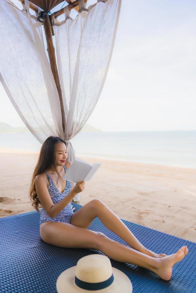 retrato, hermoso, joven, mujer asiática, libro de lectura, con, feliz, sonrisa, relajarse, en, sillón cama, en, el, playa, mar, océano, para, ocio foto