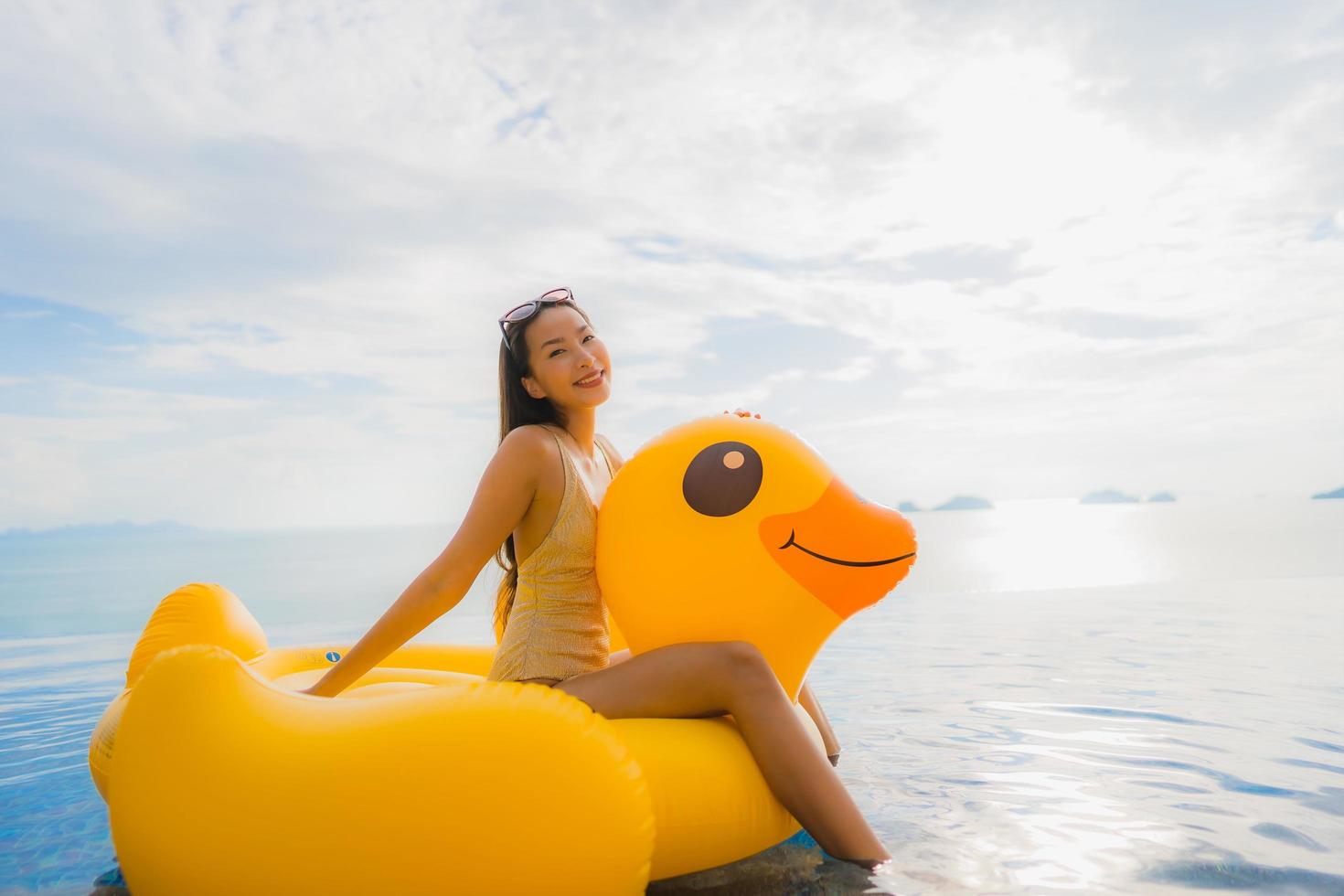 Portrait young asian woman on inflatable float yellow duck around outdoor swimming pool in hotel and resort photo