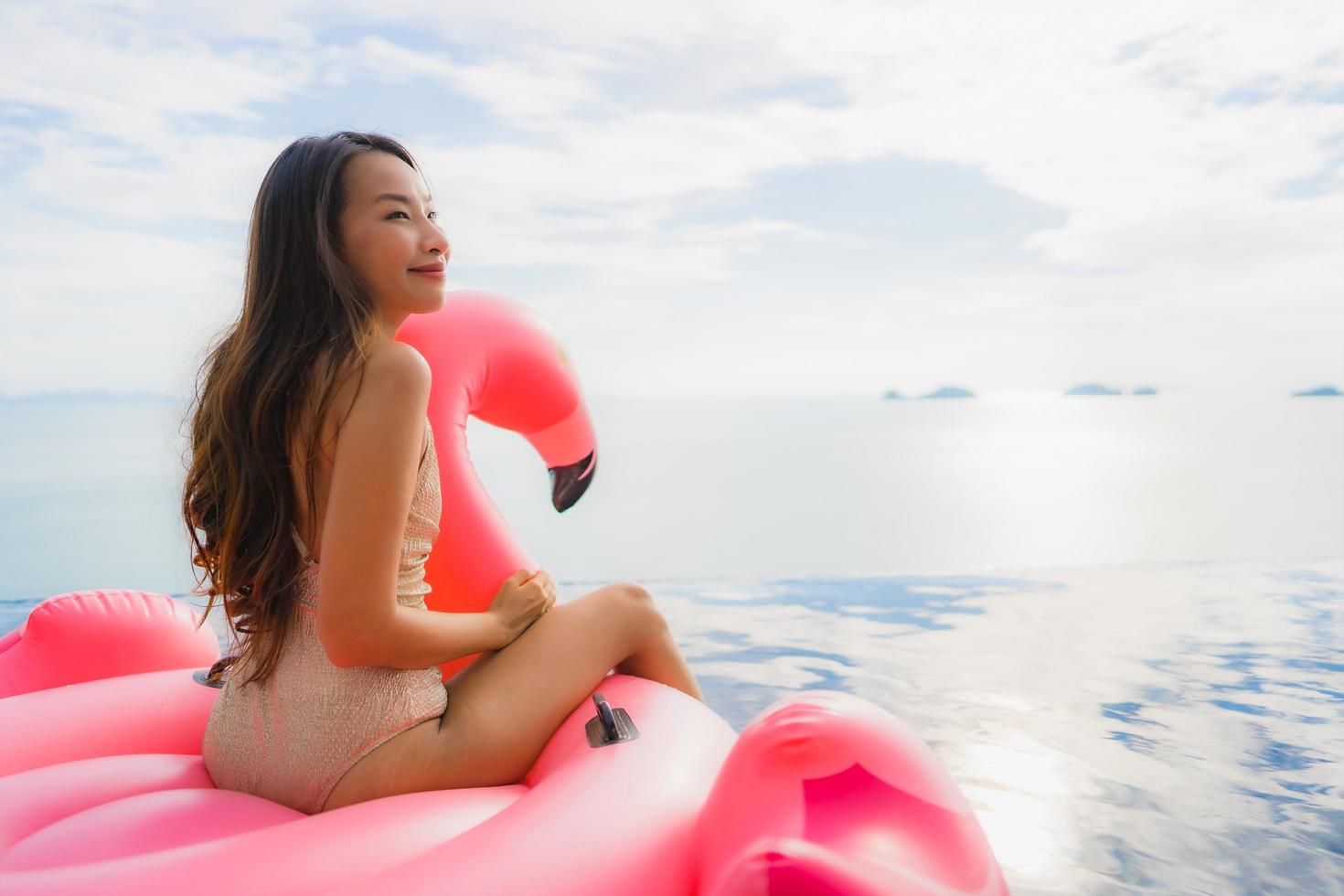 Portrait young asian woman on inflatable float flamingo around outdoor swimming pool in hotel resort photo