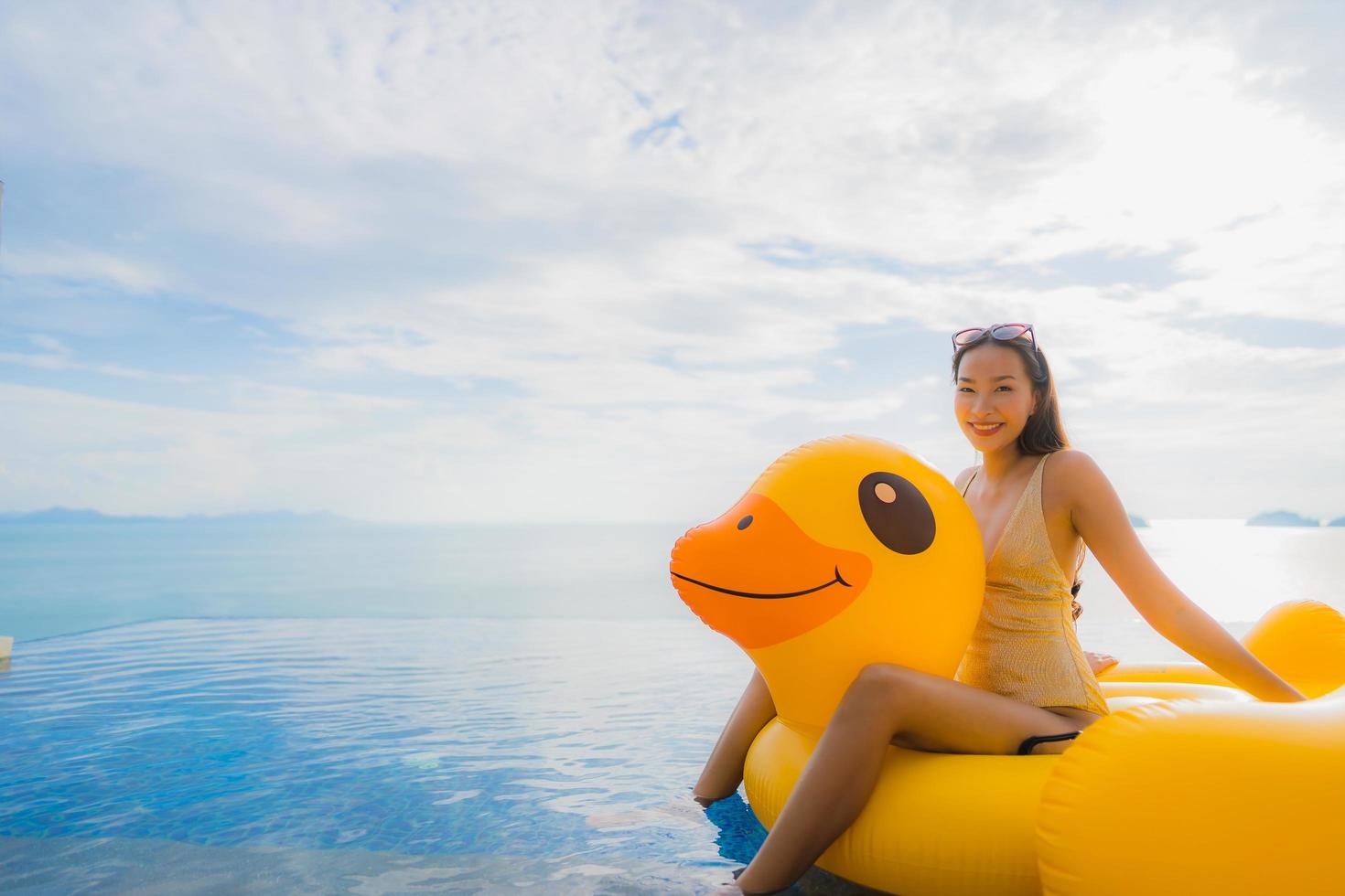 Portrait young asian woman on inflatable float yellow duck around outdoor swimming pool in hotel and resort photo