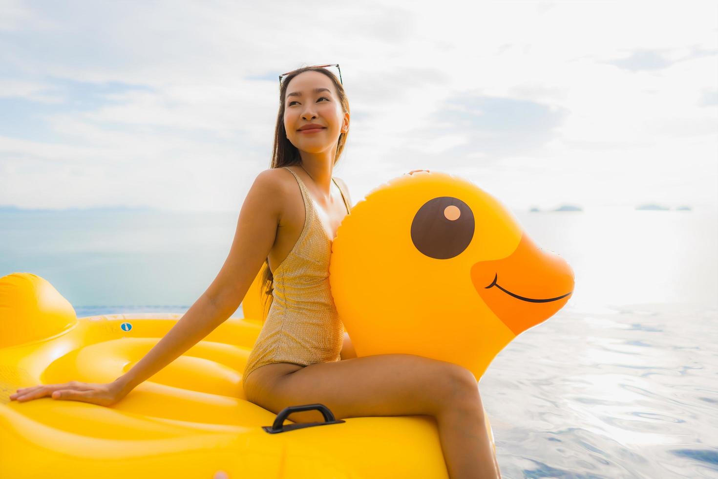 Portrait young asian woman on inflatable float yellow duck around outdoor swimming pool in hotel and resort photo