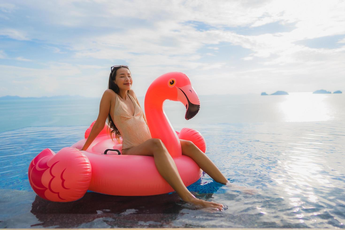 Portrait young asian woman on inflatable float flamingo around outdoor swimming pool in hotel resort photo