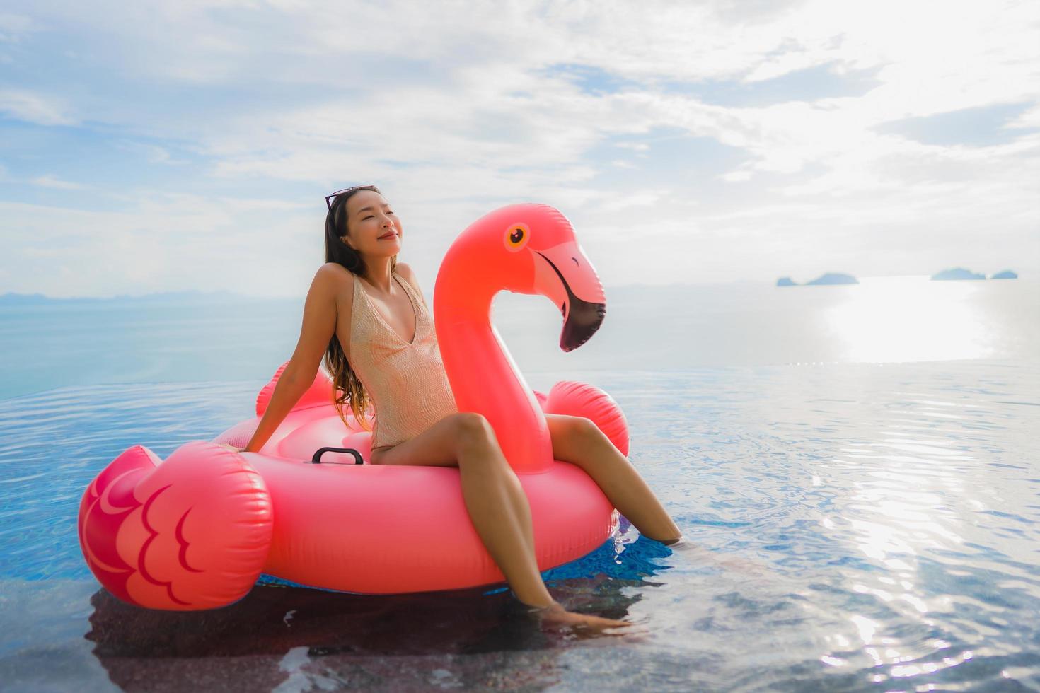 Portrait young asian woman on inflatable float flamingo around outdoor swimming pool in hotel resort photo