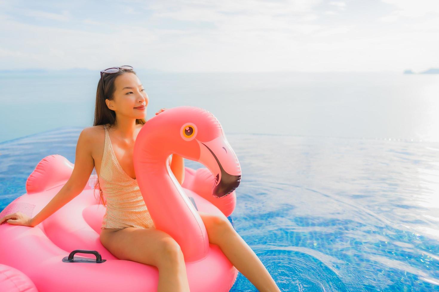 Portrait young asian woman on inflatable float flamingo around outdoor swimming pool in hotel resort photo