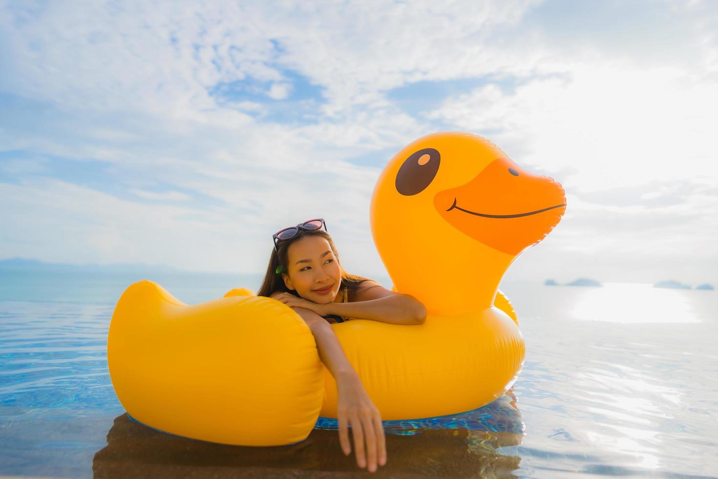 Portrait young asian woman on inflatable float yellow duck around outdoor swimming pool in hotel and resort photo