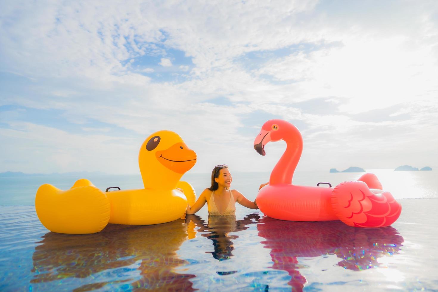 Portrait young asian woman on inflatable float yellow duck and pink flamingo around outdoor swimming pool in hotel and resort photo