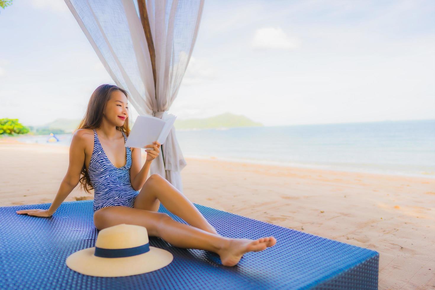 Portrait beautiful young asian woman reading book with happy smile relax in lounge bed chair on the beach sea ocean for leisure photo