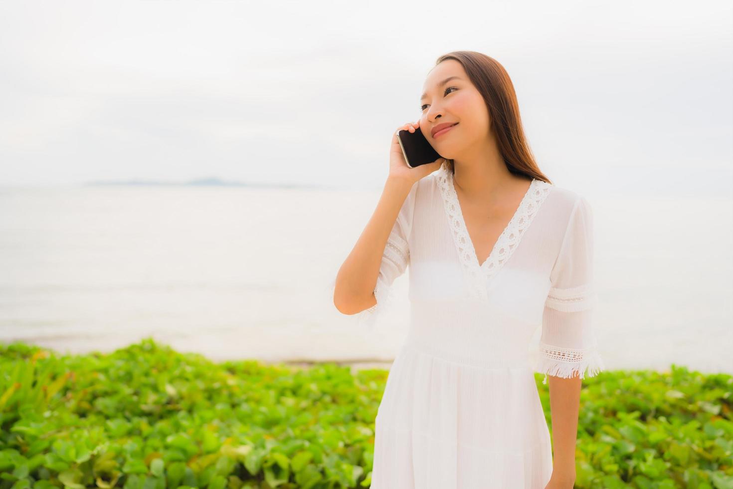 Portrait beautiful asian woman wear hat with smile happy for talking mobile phone on the beach photo