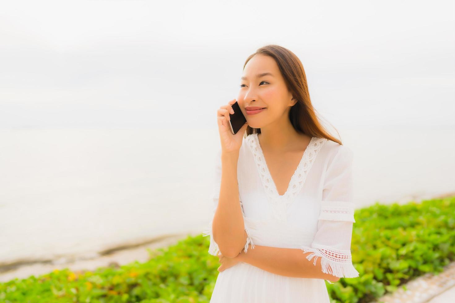 Portrait beautiful asian woman wear hat with smile happy for talking mobile phone on the beach photo