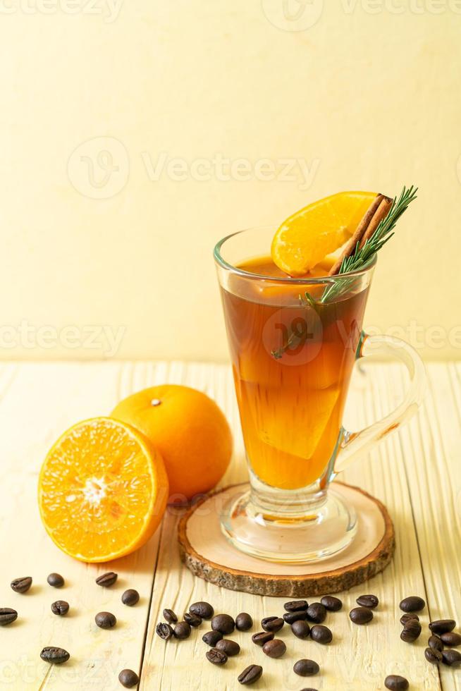 A glass of iced Americano black coffee and a layer of orange and lemon juice decorated with rosemary and cinnamon on a wood background photo