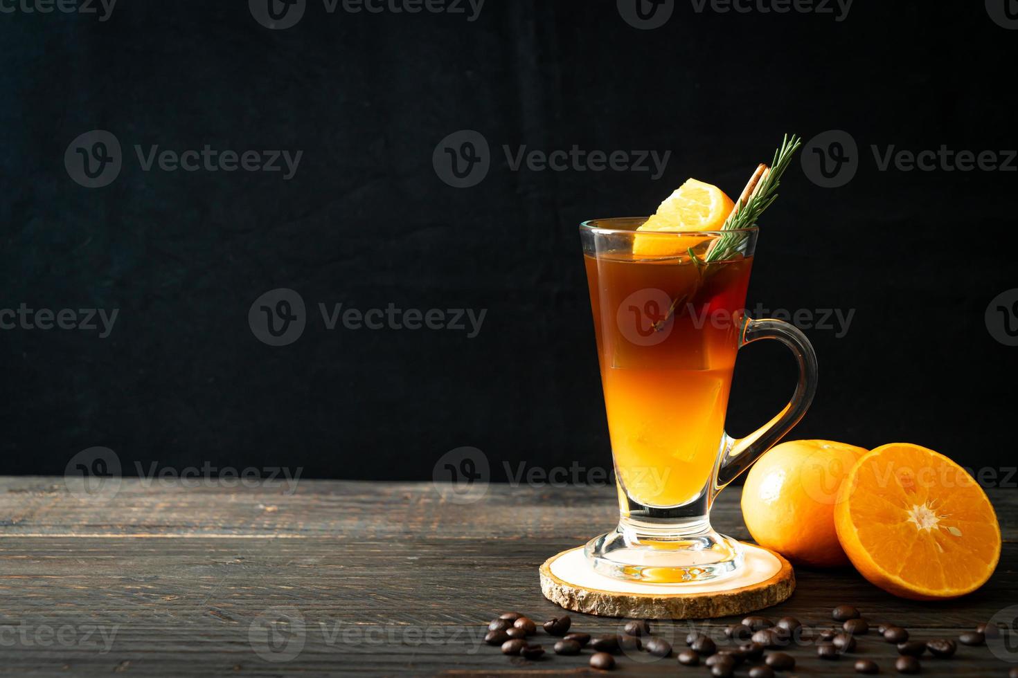 A glass of iced Americano black coffee and a layer of orange and lemon juice decorated with rosemary and cinnamon on a wood background photo