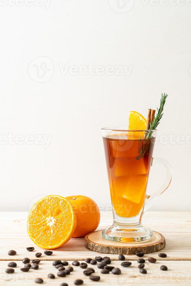 A glass of iced Americano black coffee and a layer of orange and lemon juice decorated with rosemary and cinnamon on a wood background photo