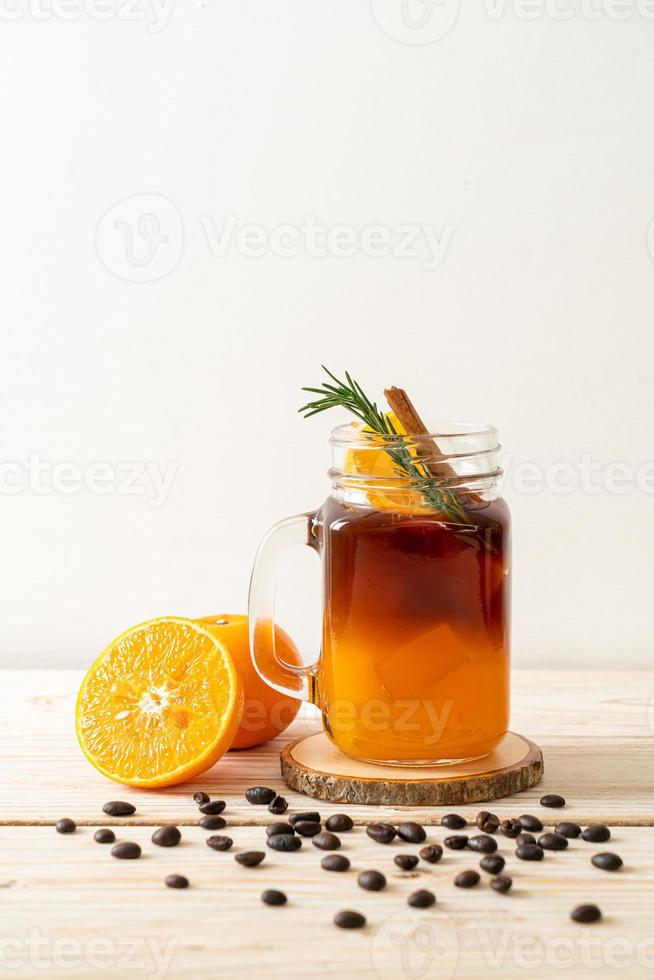 A glass of iced Americano black coffee and a layer of orange and lemon juice decorated with rosemary and cinnamon on a wood background photo