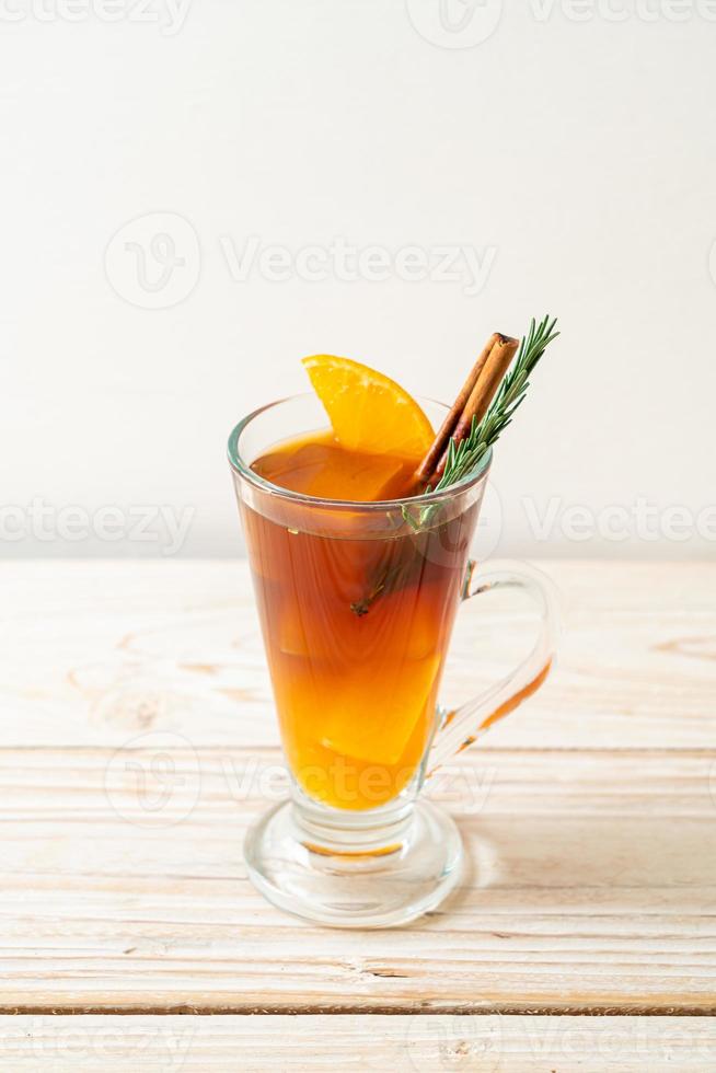 A glass of iced Americano black coffee and a layer of orange and lemon juice decorated with rosemary and cinnamon on a wood background photo