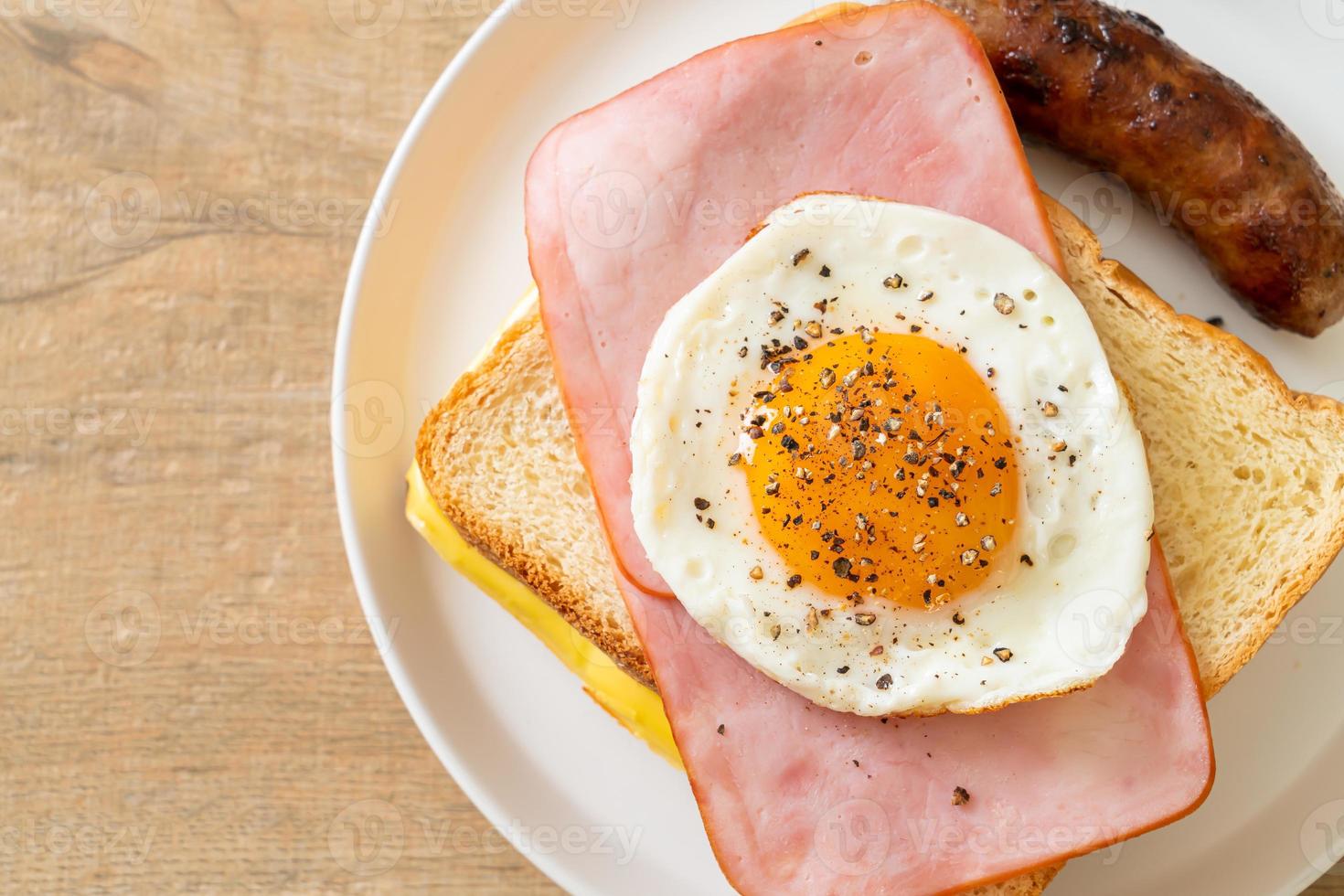 Homemade bread toasted cheese topped ham and fried egg with pork sausage for breakfast photo