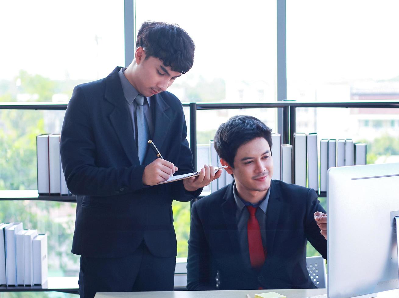 Two young business men sit and work on laptops in a modern office They are young, active businessmen photo