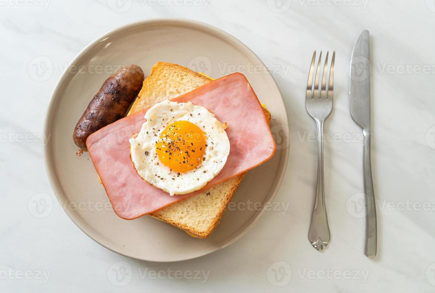 Homemade bread toasted cheese, topped ham, and fried egg with pork sausage for breakfast photo