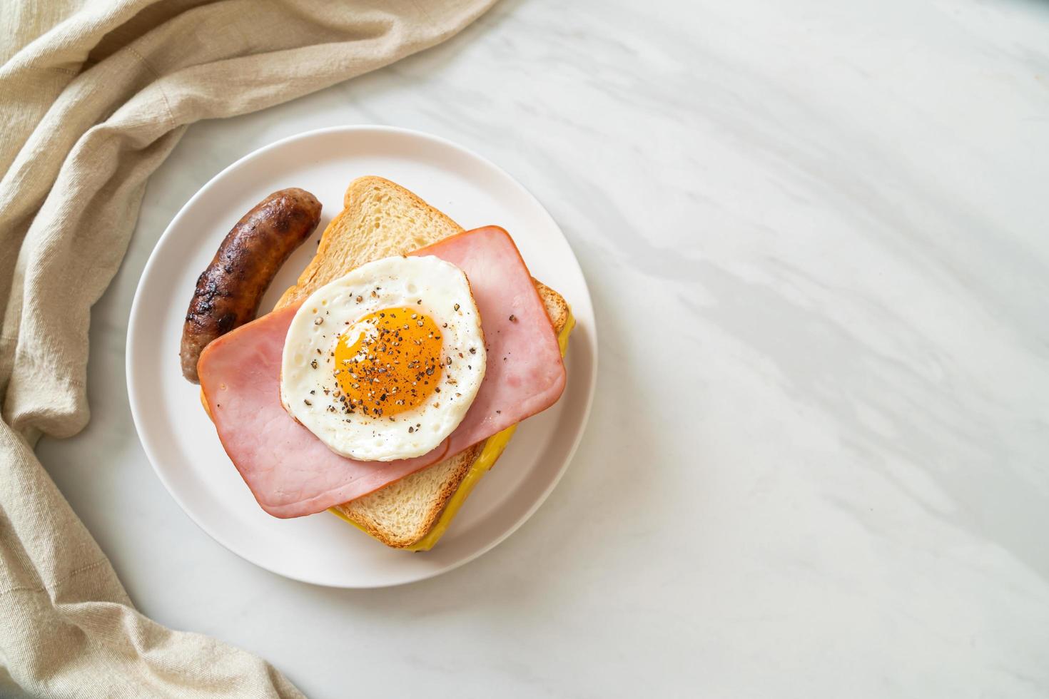 Homemade bread toasted cheese, topped ham, and fried egg with pork sausage for breakfast photo