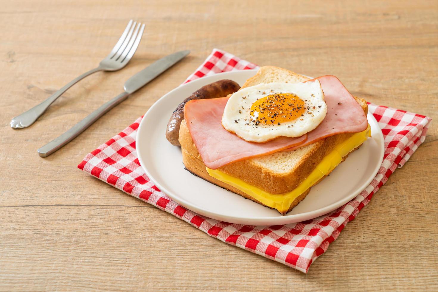 Homemade bread toasted cheese, topped ham, and fried egg with pork sausage for breakfast photo