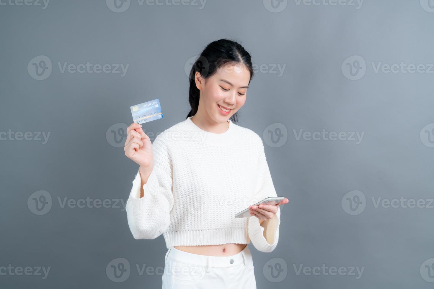 Joven asiática mostrando una tarjeta de crédito de plástico mientras sostiene el teléfono móvil foto