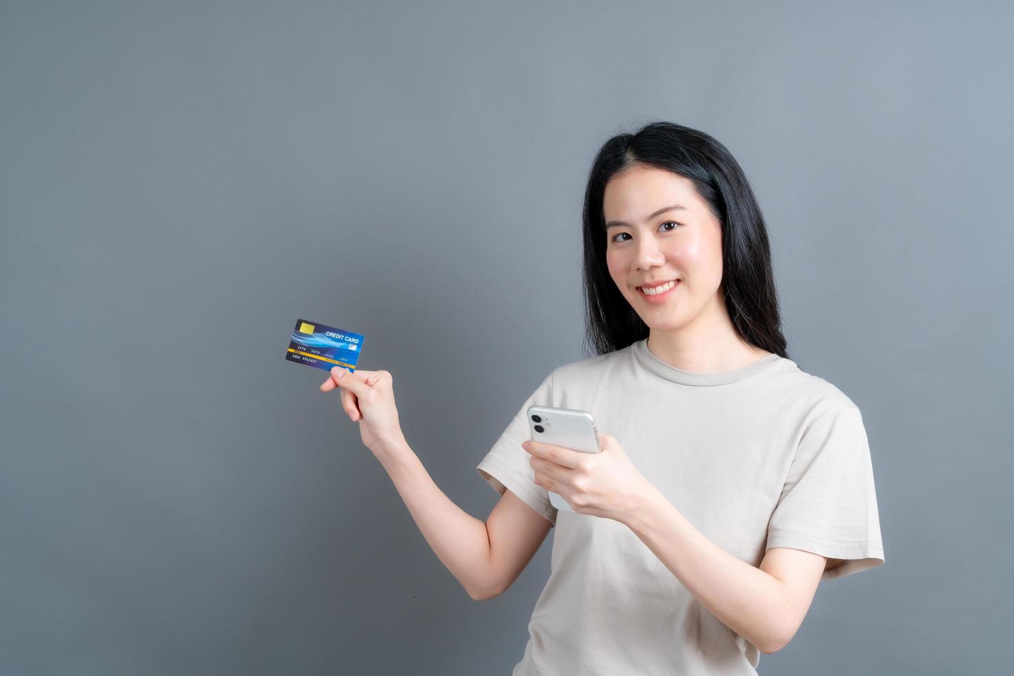 Young Asian girl showing plastic credit card while holding mobile phone photo