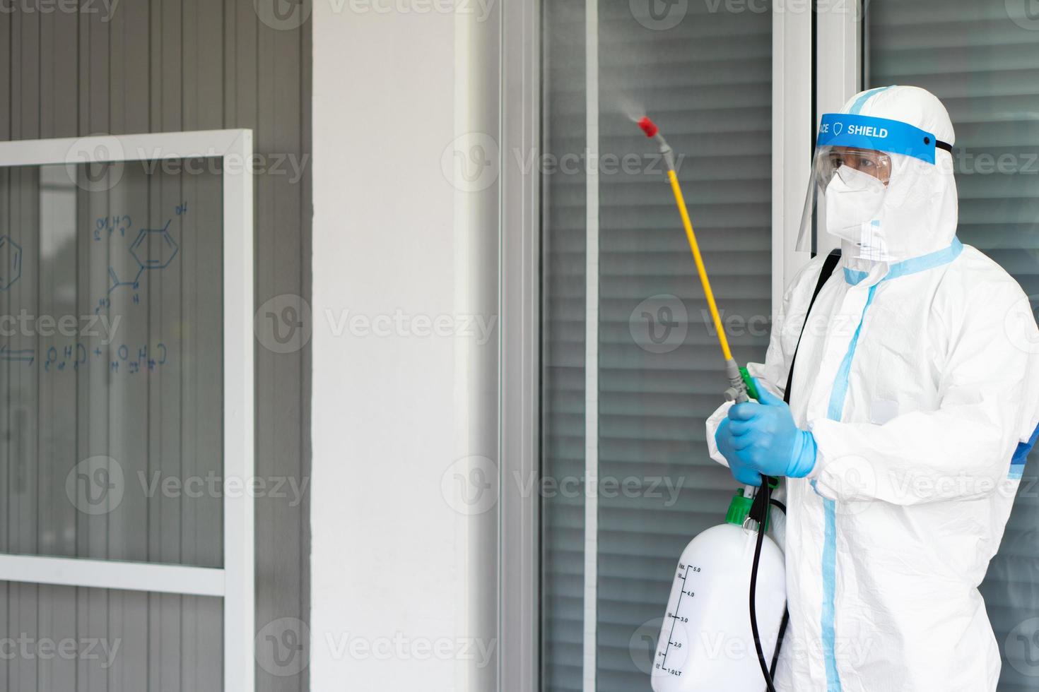 Worker from decontamination services wearing personal protective equipment or ppe including suit, face shield and mask. He uses disinfectant to spray and clean scientist lab photo