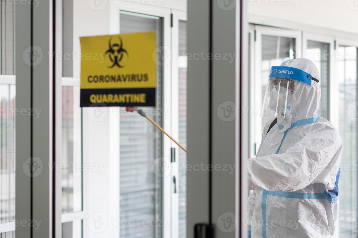 Worker from decontamination services wearing personal protective equipment or ppe including suit, face shield and mask. He uses disinfectant to spray and clean scientist lab photo