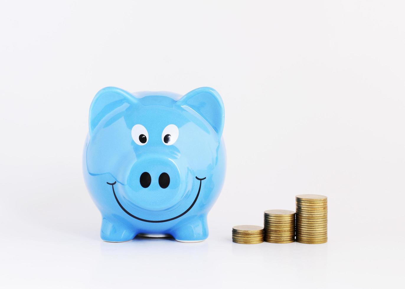Concepto de plan de ahorro con hucha azul y pila de monedas de dinero sobre fondo blanco. foto